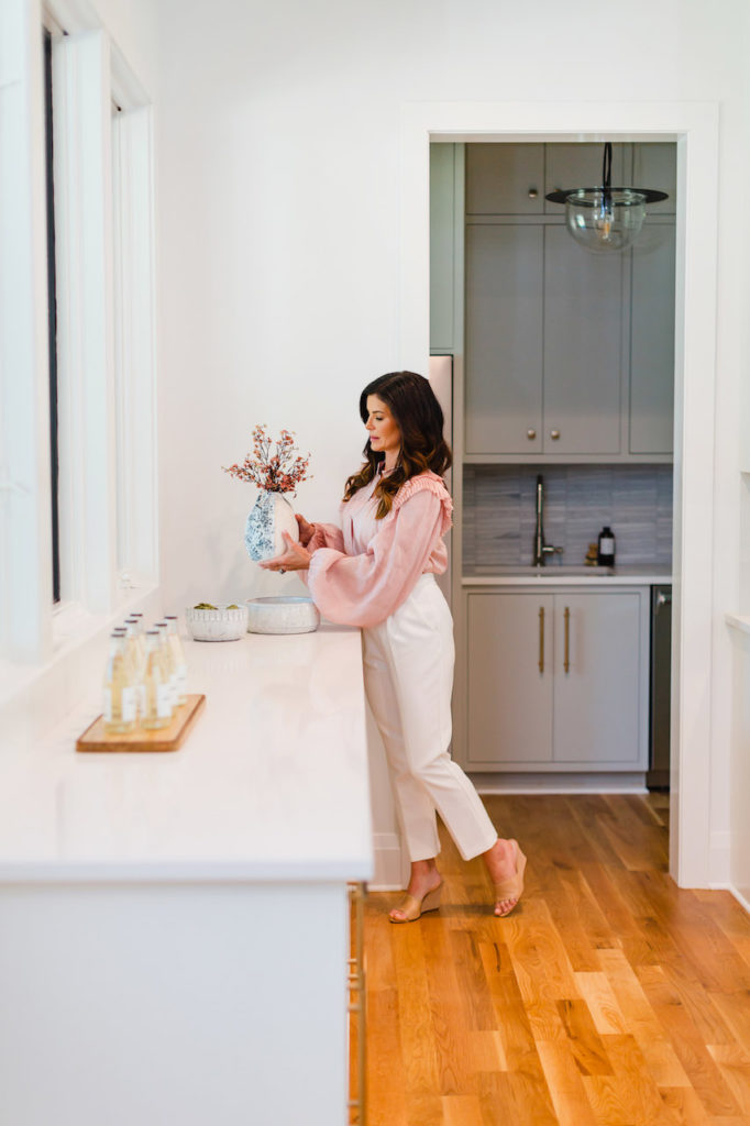 Woman placing a vase full of florals on a white marble countertop during a luxury real estate listing branding photoshoot