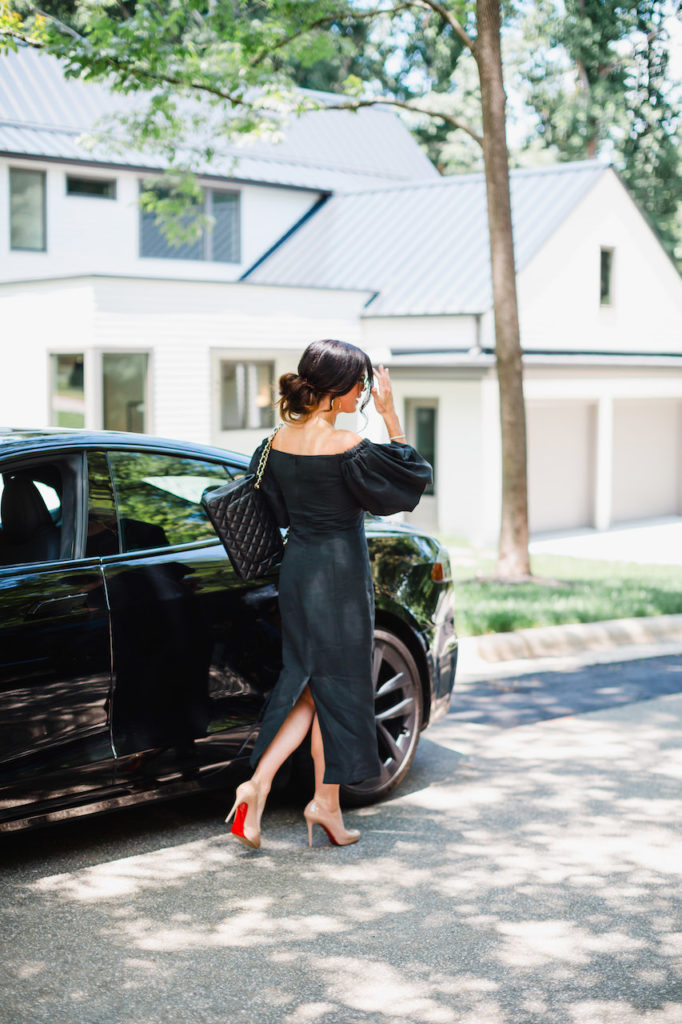 Gretchen Coley real estate agent wearing a black dress and walking in front of a black car on the road outside of a premium real estate listing in Raleigh NC