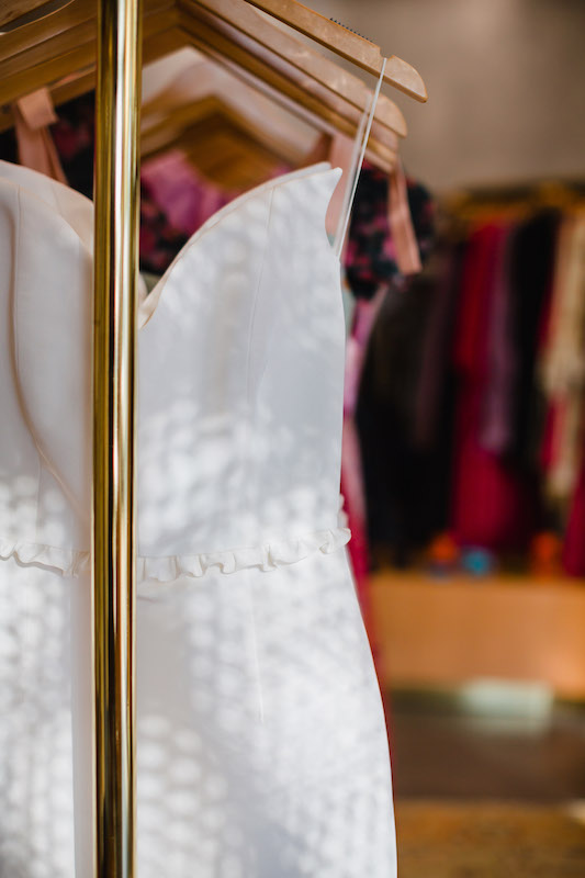 Close up image of a white dress hanging on a wooden hanger on a gold clothing rack | Sara Coffin Photography