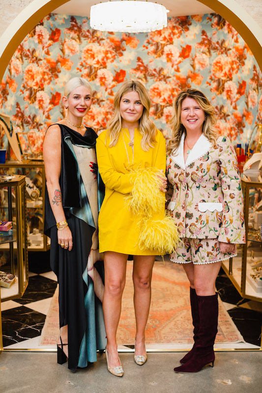 Three women in bold print outfits stand under arched doorway in front of a floral patterned wall inside an upscale clothing boutique | Sara Coffin Photography