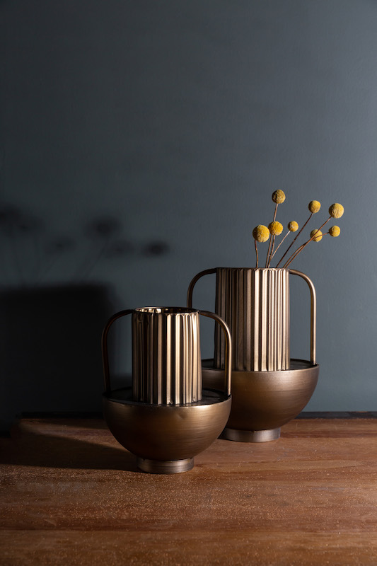 Two Werking Design & Decor brass carved vases with handles sitting on a wooden floor against a slate gray backdrop | Small Business Product Photography by Sara Coffin Photography