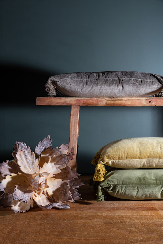 Wooden bench holding velvet pillow sitting on a wooden floor against a slate gray backdrop | Small Business Product Photography by Sara Coffin Photography