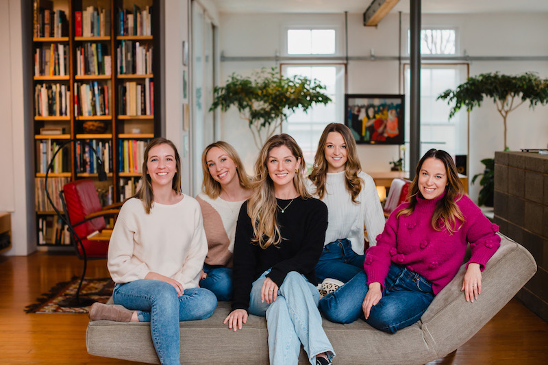 Five women sit on a couch and pose for a team photo session | Sara Coffin Photography