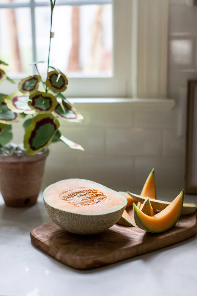 A sliced cantaloupe sits on a wooden cutting board in front of a window | Interior Design detail by Lindsay Speace Interiors Photographed by Interior Photographer Sara Coffin Photo