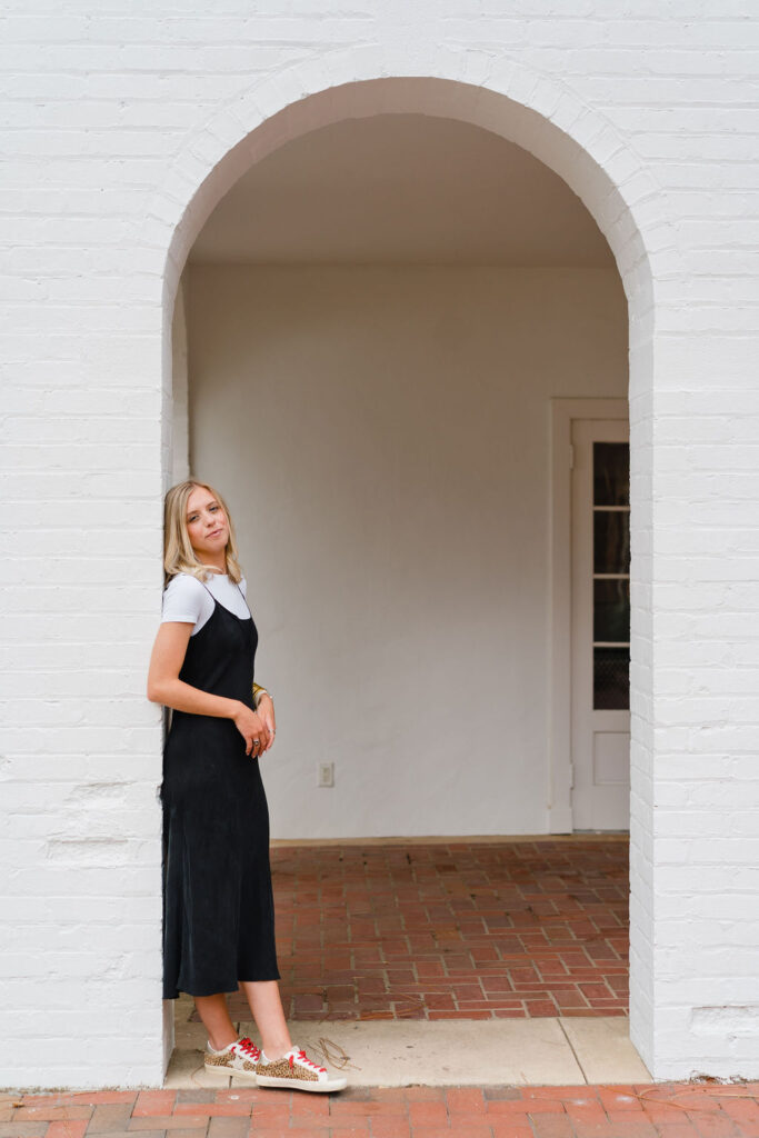 Girl in a black slip dress leans against a brick archway on the terrace of the Boyd House at Weymouth Center in Southern Pines NC | Photo by Sara Coffin Photography