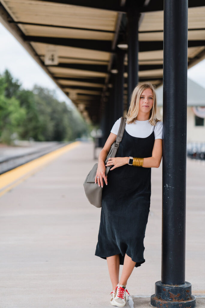 Girl in black slip dress leans against train station stop in Southern Pines NC