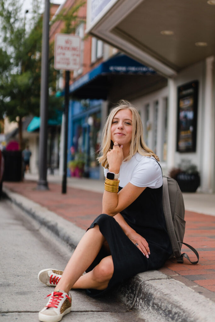 Girl in black slip dress sits on the curb in front of the Sunrise Theater in downtown Southern Pines