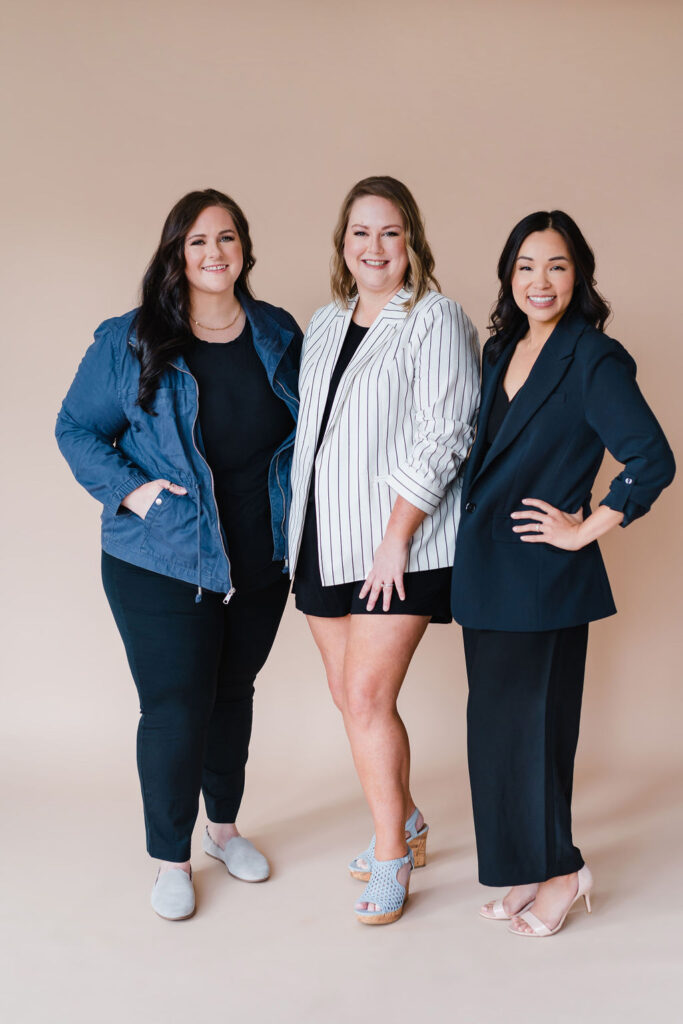 Team of three eye doctors pose in front of a tan photo backdrop for The Vision Studio business branding photography by Sara Coffin