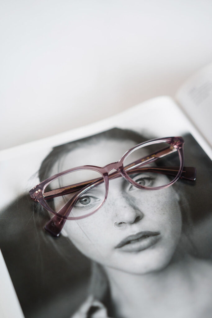 Pair of clear pink eyeglasses sits on top of a magazine photo of a woman