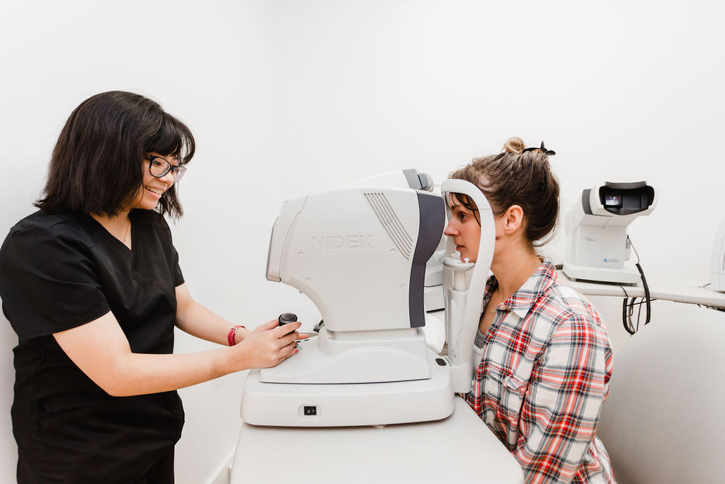 Female eye doctor operates machinery while patient sits across from her and looks into a retinal scanner