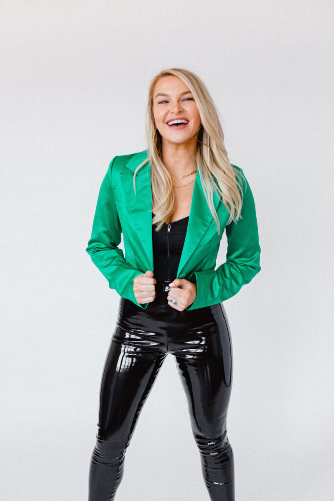 Woman wears shiny black leather pants with a satin kelly green blazer outfit for headshots inside a photo studio in NC
