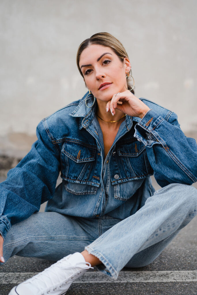 Model wears cropped denim jacket over a denim shirt and light wash denim jeans with white high top converse