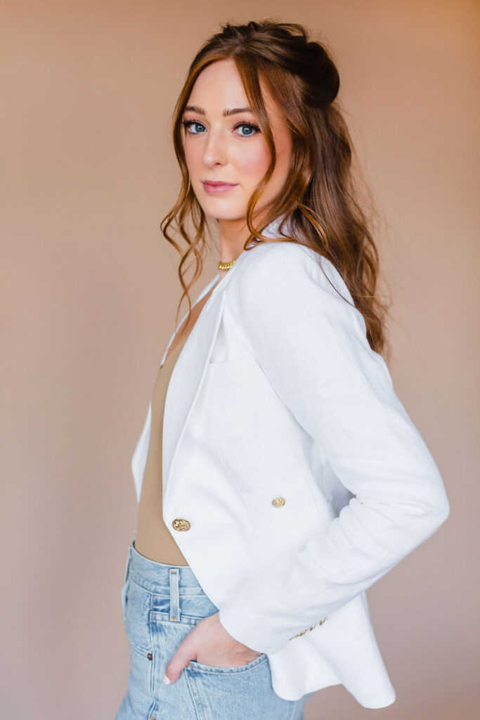Woman wears white blazer outfit for headshots and smiles at the camera during a personal branding photoshoot