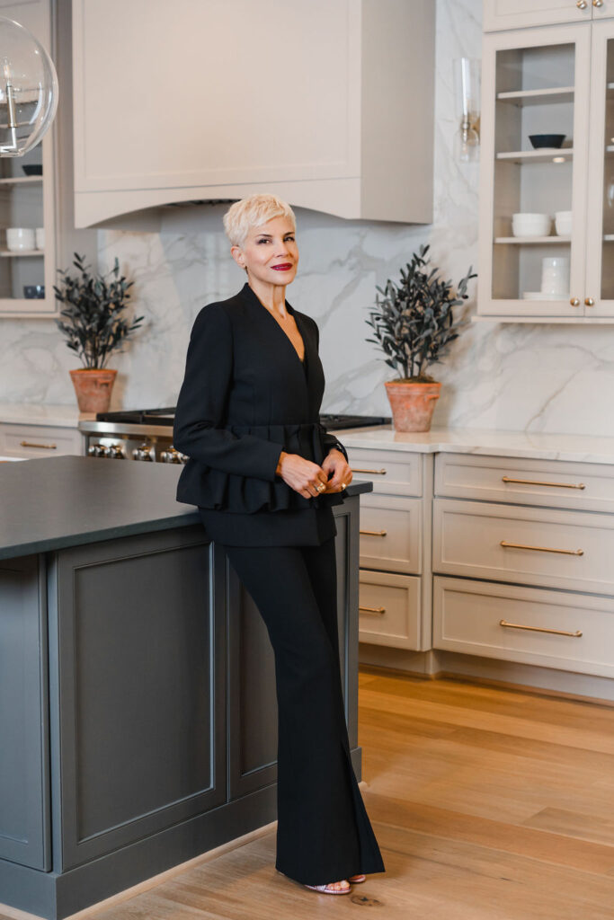 Woman in a black two piece suit leans back against charcoal gray kitchen island | Personal branding photoshoot for realtor Marianne Mansour