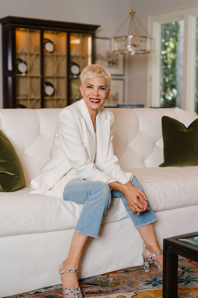 Woman wearing a white blazer and jeans sits on a white tufted couch | Personal branding photoshoot for realtor Marianne Mansour