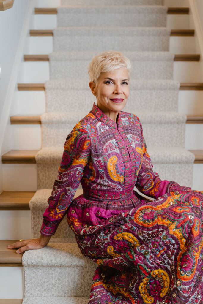 Woman in a long sleeved pink paisley dress sits on a carpet covered wood staircase | Personal branding photoshoot for realtor Marianne Mansour