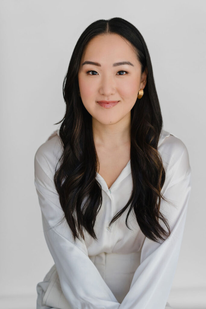Asian woman sits in front of a white backdrop wearing a white silk blouse for a professional headshot | Sara Coffin Photo Headshot Mini Marathon session experience