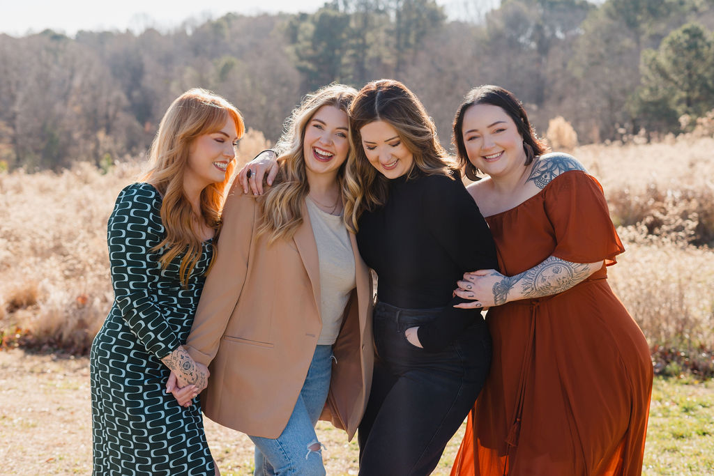 Group of four women stand together in a field while smiling and laughing | Sara Coffin Photo