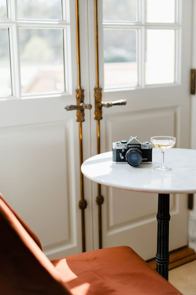 Film camera sits on marble top cafe table next to a burnt orange velvet chair at Oxbow Estate in Clayton, NC | Sara Coffin Photo