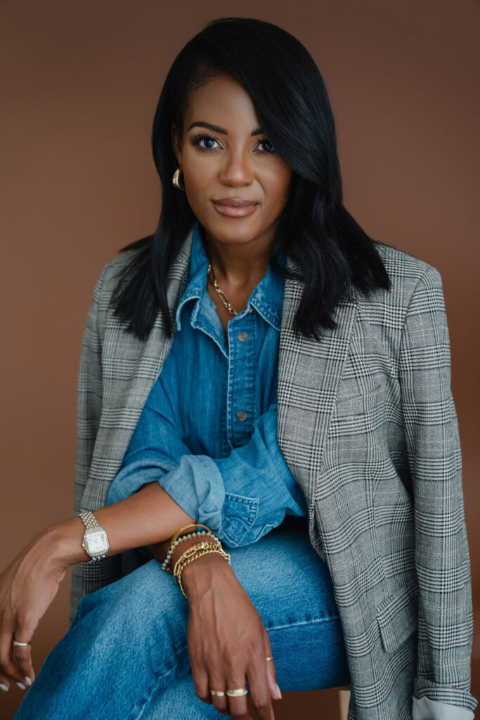 Black female entrepreneur poses in a gray plaid blazer and denim shirt combo with straight leg jeans in front of a brown backdrop inside a North Carolina photo studio | Sara Coffin Photo