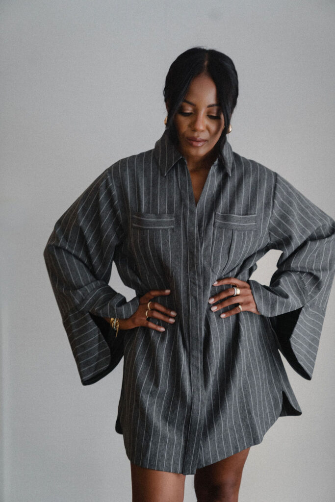 Black female entrepreneur wearing charcoal gray pinstripe oversized shirt dress poses with hands on her hips inside a North Carolina photo studio | Portrait photography by Sara Coffin Photo