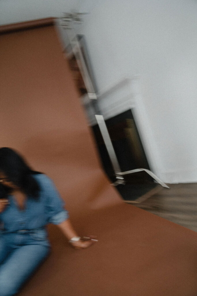 Motion blur photo of a black female entrepreneur posing in a gray plaid blazer and denim shirt combo with straight leg jeans while sitting on a brown paper backdrop inside a North Carolina photo studio | Sara Coffin Photo