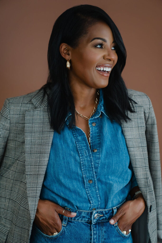 Black female entrepreneur poses in a gray plaid blazer and denim shirt combo with straight leg jeans in front of a brown backdrop inside a North Carolina photo studio | Sara Coffin Photo