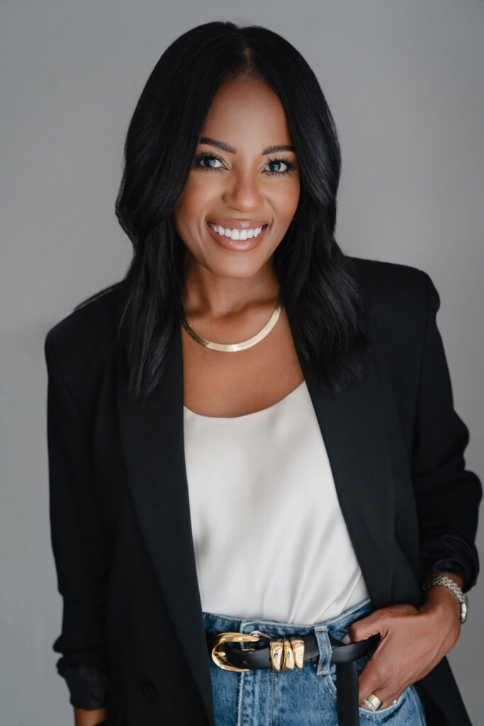 Black female entrepreneur poses in a black blazer and white shirt combo with straight leg jeans inside a North Carolina photo studio | Sara Coffin Photo