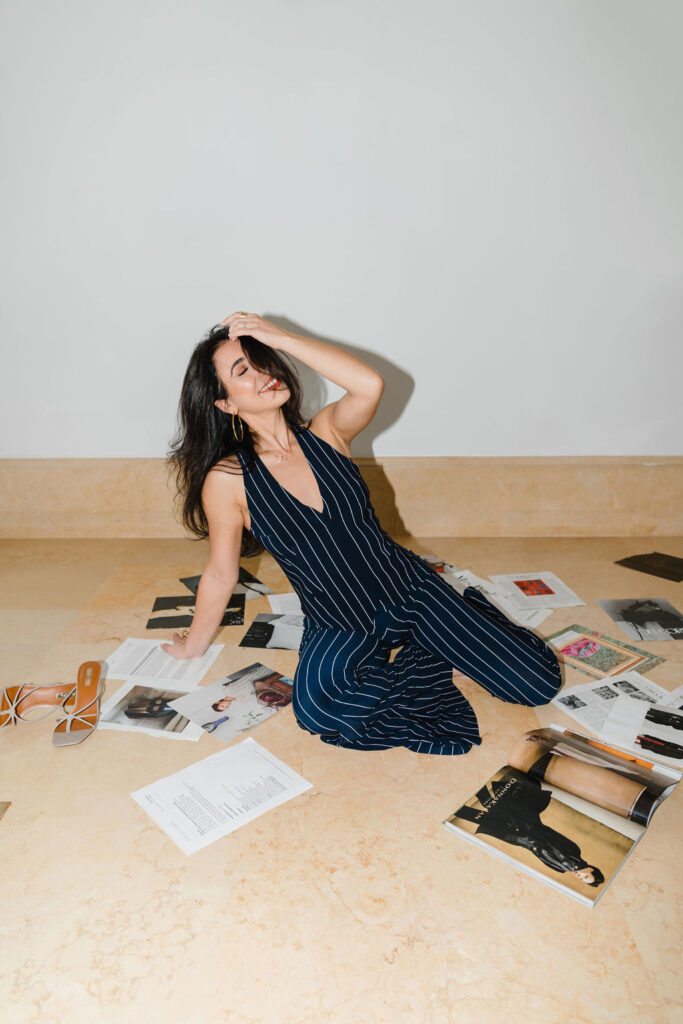 Brunette woman in navy and white striped matching set outfit poses on the marble floor at Oxbow Estate in Clayton, NC surrounded by fashion magazine pages during Sara Coffin Photo branding session | photoshoot hair and makeup tips